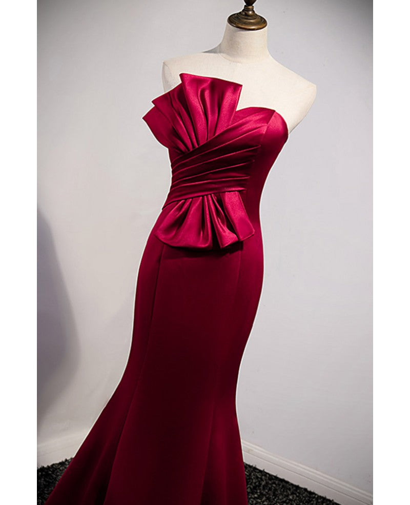 Un abito da ballo rosso vino nobile e minimalista, senza maniche, con spalle scoperte, spalline senza spalline e schiena color rosso vino e abito da sera a sirena lungo fino a terra.